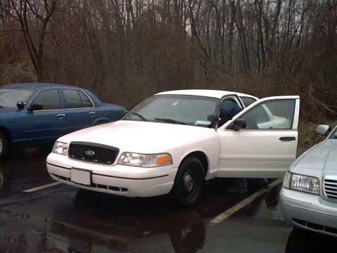 2000 Ford Crown Victoria - Three-quarter front view of a white Ford Crown Victoria P71 police-package sedan parked on wet pavement with both passenger doors open and…