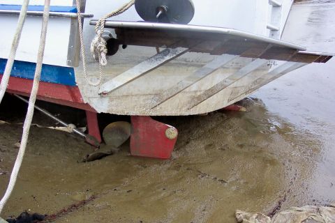 1985 Carver 326 Aft Cabin - Stern view of a grounded boat with its propeller and rudder visible in the mud.