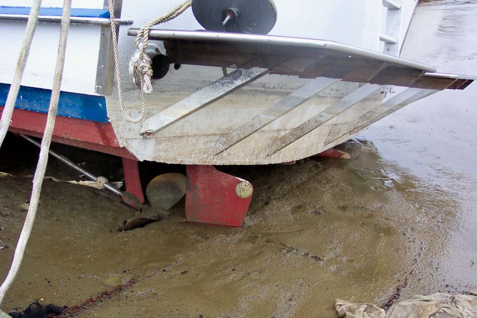 Boat stern with bronze propeller and red rudder resting on mud at low tide