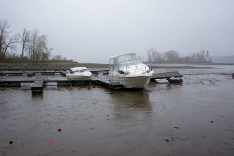 1985 Carver 326 Aft Cabin - Two boats sit stranded on a muddy shoreline with docks extending into the shallow water.