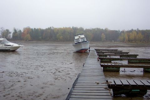 1985 Carver 326 Aft Cabin - A boat is beached on a muddy shore next to a dock, with another boat visible in the background.
