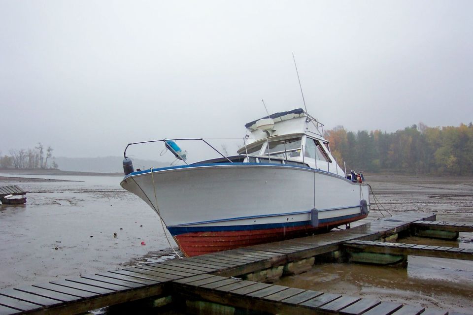 White cabin cruiser with blue trim and red hull bottom grounded on mud beside wooden docks