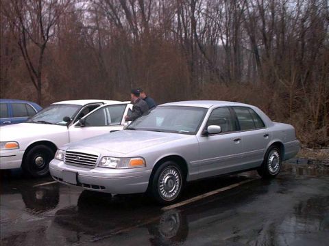 2000 Ford Crown Victoria - Three-quarter front view of a silver Ford Crown Victoria sedan on wet pavement, wearing chrome-look turbine-style wheel covers and body-col…