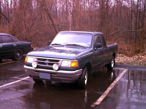 2000 Ford Crown Victoria - A dark blue Ford Ranger pickup truck is parked in a lot next to a dark sedan, with trees in the background.