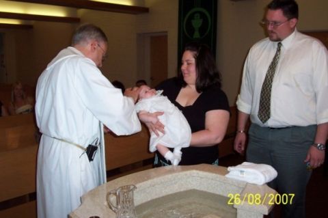 2000 Ford Crown Victoria - A baptism ceremony takes place with a priest, a mother holding her baby, and a man observing.