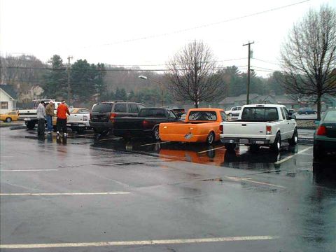 2000 Ford Crown Victoria - An orange Ford Ranger pickup truck with flame decals on its bed is parked in a wet parking lot.