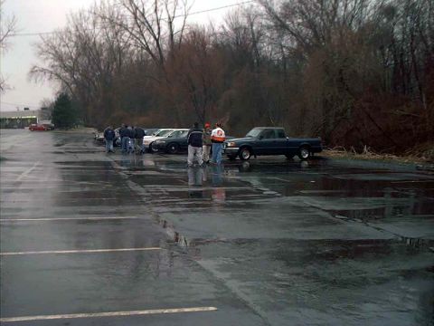 2000 Ford Crown Victoria - Several vehicles gathered in a wet parking lot on an overcast day.
