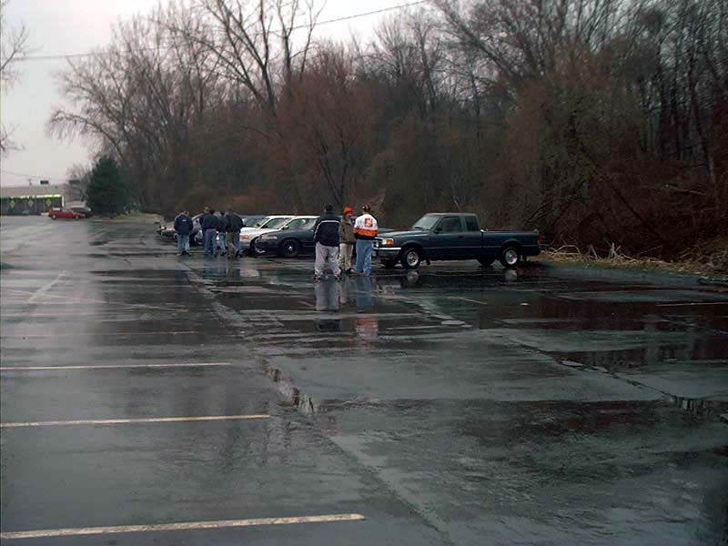 Parking lot scene with multiple cars and a dark blue pickup truck, wet pavement