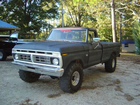 1986 Ford Bronco - A black 1973 Ford F-150 pickup truck is shown from a 3/4 front angle, parked on a gravel surface with trees in the background.