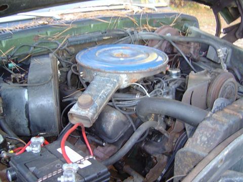 1986 Ford Bronco - The engine bay of a vehicle, showing the V8 engine components and battery, with debris on top.