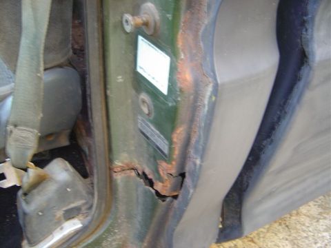 1986 Ford Bronco - Detail of a rusted door frame and seatbelt, showing significant corrosion.