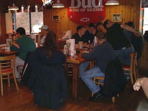 2000 Ford Crown Victoria - A group of people are seated at tables in a casual dining establishment, with wood paneling and bar-style decor visible.