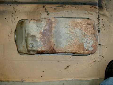 1996 Ford Bronco - A heavily rusted oil pan is shown from a top-down perspective on a cardboard surface.