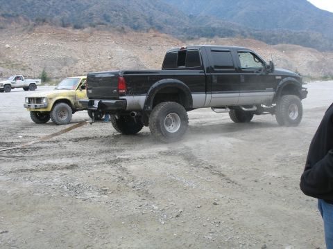 1987 Ford Bronco - Two pickup trucks are parked in a dusty, outdoor environment with mountains in the background.