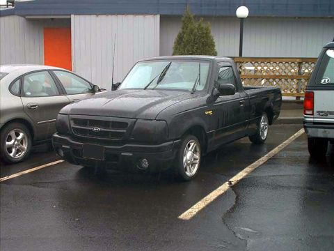 2000 Ford Crown Victoria - A black Ford Ranger pickup truck is parked next to another vehicle on a wet day.