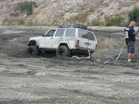 1987 Ford Bronco - A white Jeep Cherokee is stuck in thick mud, with a man observing the situation.