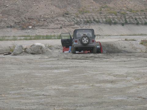 1987 Ford Bronco - Two vehicles are stuck in a sandy area with a rocky hillside in the background.