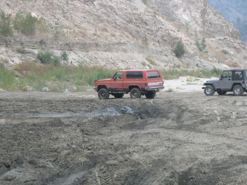 1987 Ford Bronco - A red SUV and a gray Jeep are parked on a muddy, rocky landscape near a hillside.