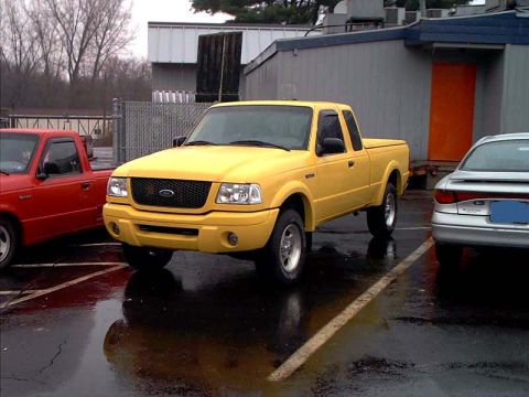 2000 Ford Crown Victoria - A yellow Ford Ranger pickup truck is parked next to a red Ford Ranger and a silver sedan.
