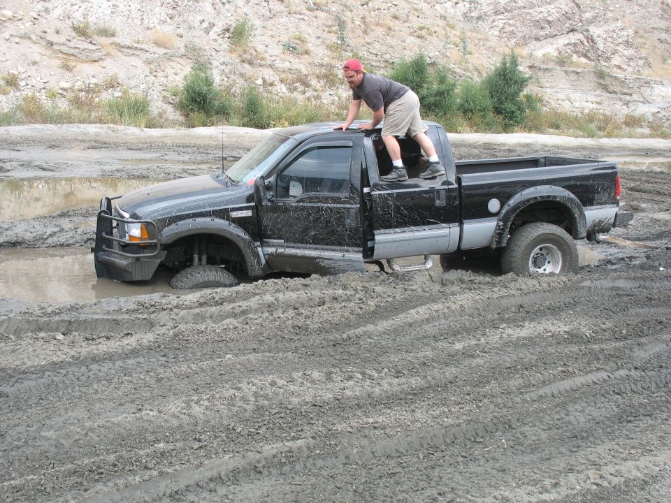 Black pickup truck stuck in mud with a man on its roof