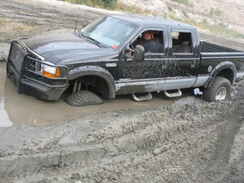 1987 Ford Bronco - This black pickup truck is deeply stuck in mud, with its front wheel submerged.