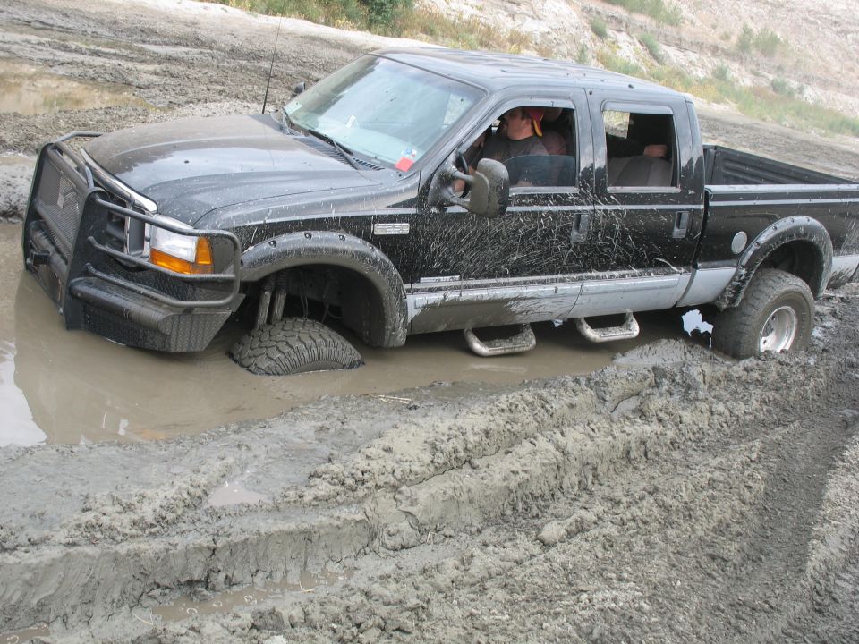 Black pickup truck stuck in mud, front wheel deep