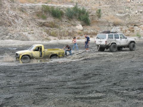 1987 Ford Bronco - Two vehicles are stuck in thick mud while people attempt to free them.