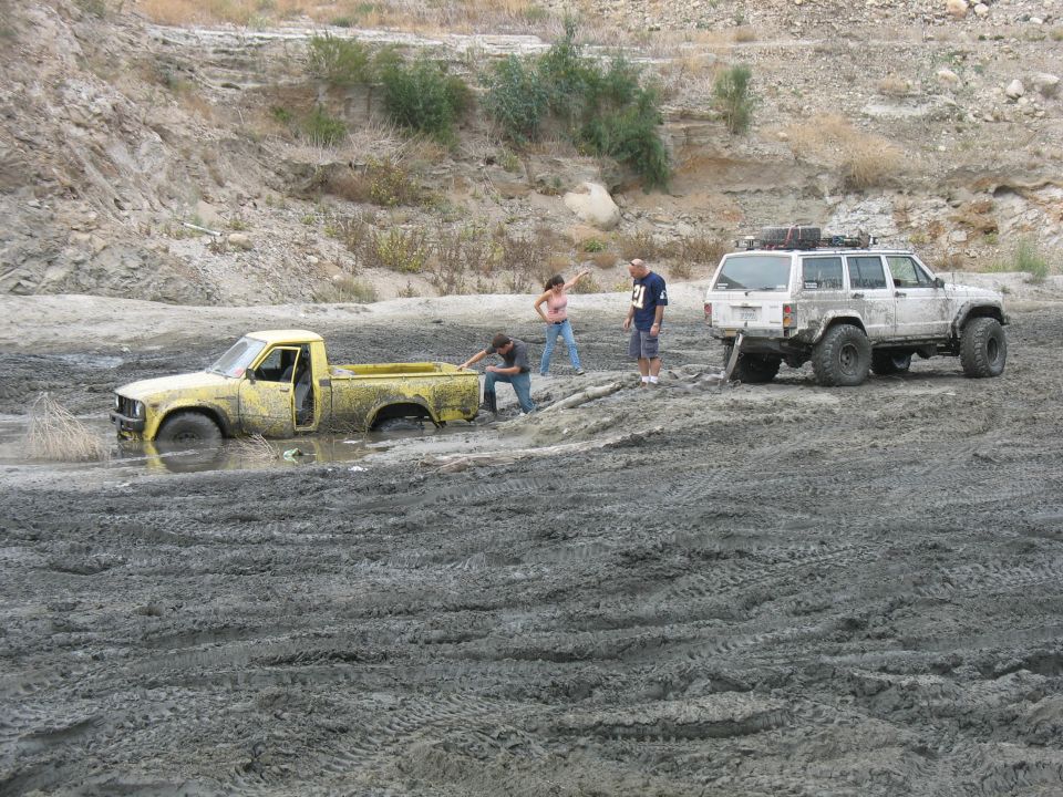 Yellow pickup truck stuck in mud, white SUV nearby, people trying to help