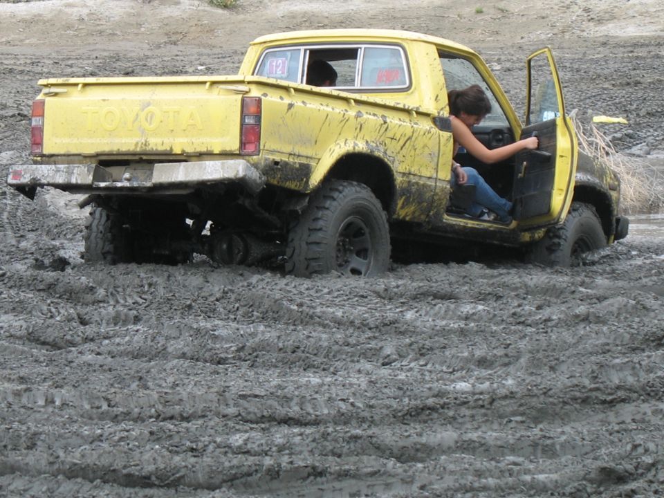 Yellow Toyota pickup truck stuck deep in mud, driver's door open