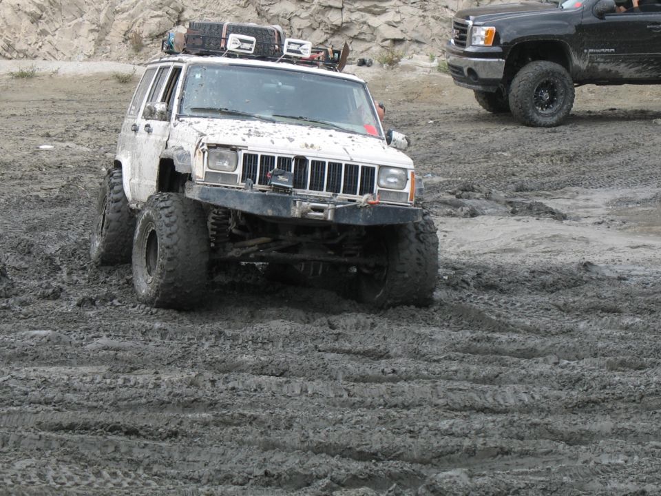 White Jeep Cherokee XJ with off-road tires and roof rack driving in mud
