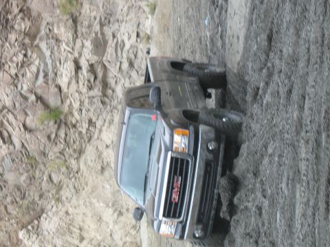 1987 Ford Bronco - A GMC pickup truck is stuck on a steep dirt embankment, with its front end angled upwards.