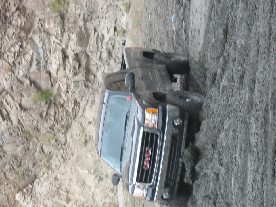GMC pickup truck with front grille and headlights visible, stuck on a dirt embankment