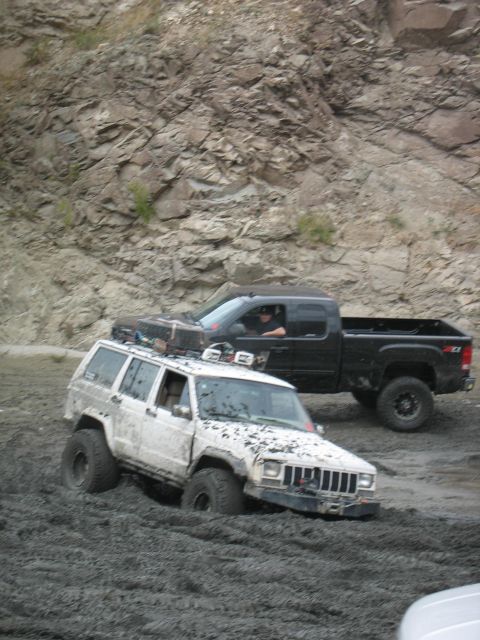 1987 Ford Bronco - Two off-road vehicles navigate a muddy terrain, with the white Jeep Cherokee deeply mired.