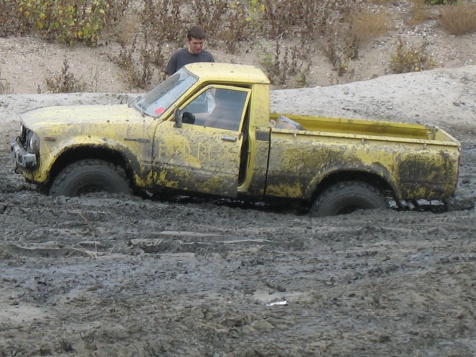 Yellow pickup truck stuck deep in mud, driver looking on