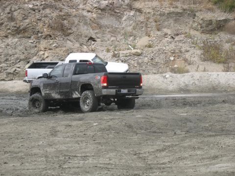 1987 Ford Bronco - A black GMC Sierra pickup truck is stuck in the mud, with another white truck visible behind it in a rocky, outdoor setting.