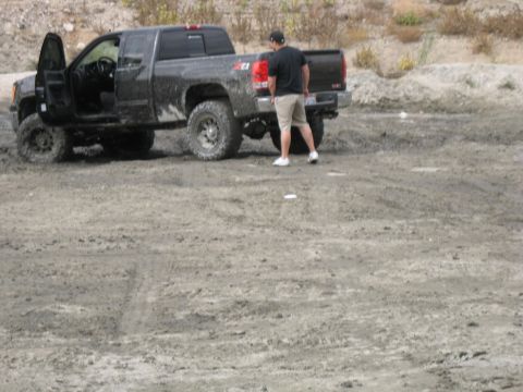 1987 Ford Bronco - A black pickup truck with off-road tires sits in a dirt lot, driver's door ajar.