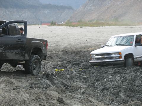 1987 Ford Bronco - Two trucks are stuck in a muddy area, with one partially submerged.