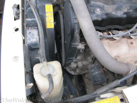 1987 Suzuki Samurai - Close-up view of the engine bay, showing the radiator, fan, and various hoses and belts. An oil filter is also visible.