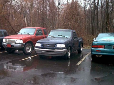 2000 Ford Crown Victoria - Two Ford Ranger pickup trucks are parked in a lot on a cloudy day, with bare trees in the background.