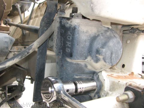 1987 Suzuki Samurai - Close-up under a Suzuki Samurai showing a cast metal component (likely a differential or transmission/transfer case) marked with raised tex…