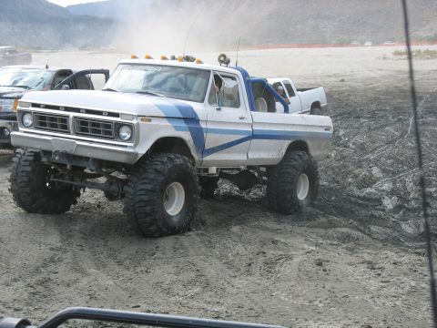 1987 Ford Bronco - This lifted Ford pickup truck is equipped with large off-road tires and appears to be navigating a muddy terrain.