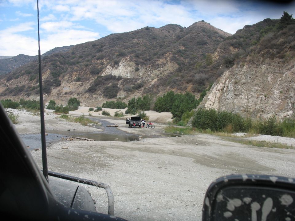 Truck and motorcycle parked near a stream in a mountainous, dry riverbed