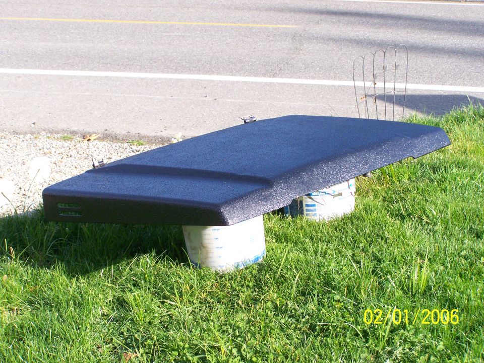 Black textured hardtop or panel propped on buckets on grass beside a roadway