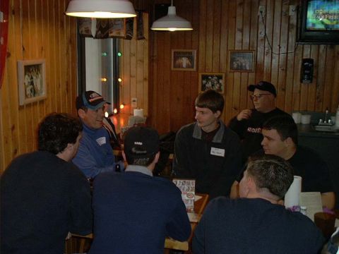 2000 Ford Crown Victoria - A group of men wearing name-tag stickers sit around tables at a wood-paneled Hooters restaurant, talking under hanging pendant lamps with f…