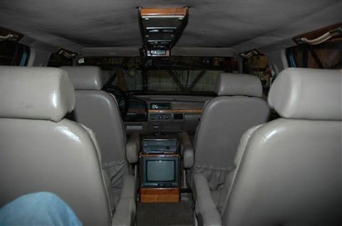 1995 Ford C-350 (Centurion Conversions) - The interior of a van shows beige seats, a dashboard with a radio, and a television set.