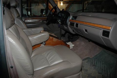 1995 Ford C-350 (Centurion Conversions) - The interior features tan leather captain's chairs, wood trim accents on the dashboard, and a rubber floor mat.