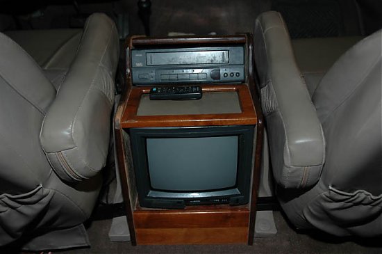Wood center console with CRT TV and VHS player between gray leather seats in a van conversion