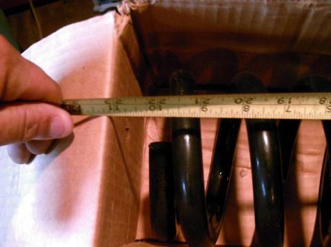 1986 Ford Bronco - A tape measure is used to measure the diameter of a black coil spring, which is inside a cardboard box.