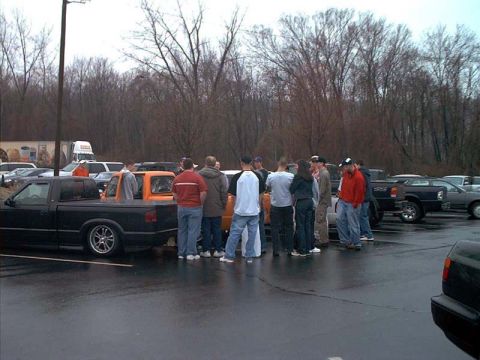 2000 Ford Crown Victoria - Wet parking-lot meet on an overcast winter day: a crowd of people stands between a lowered black regular-cab mini truck on polished five-sp…