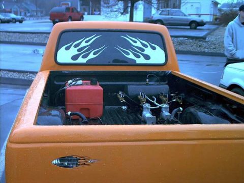 2000 Ford Crown Victoria - Looking into the bed of an orange mini truck at an air-ride setup: a red portable fuel jug and a black air tank with brass fittings and pai…